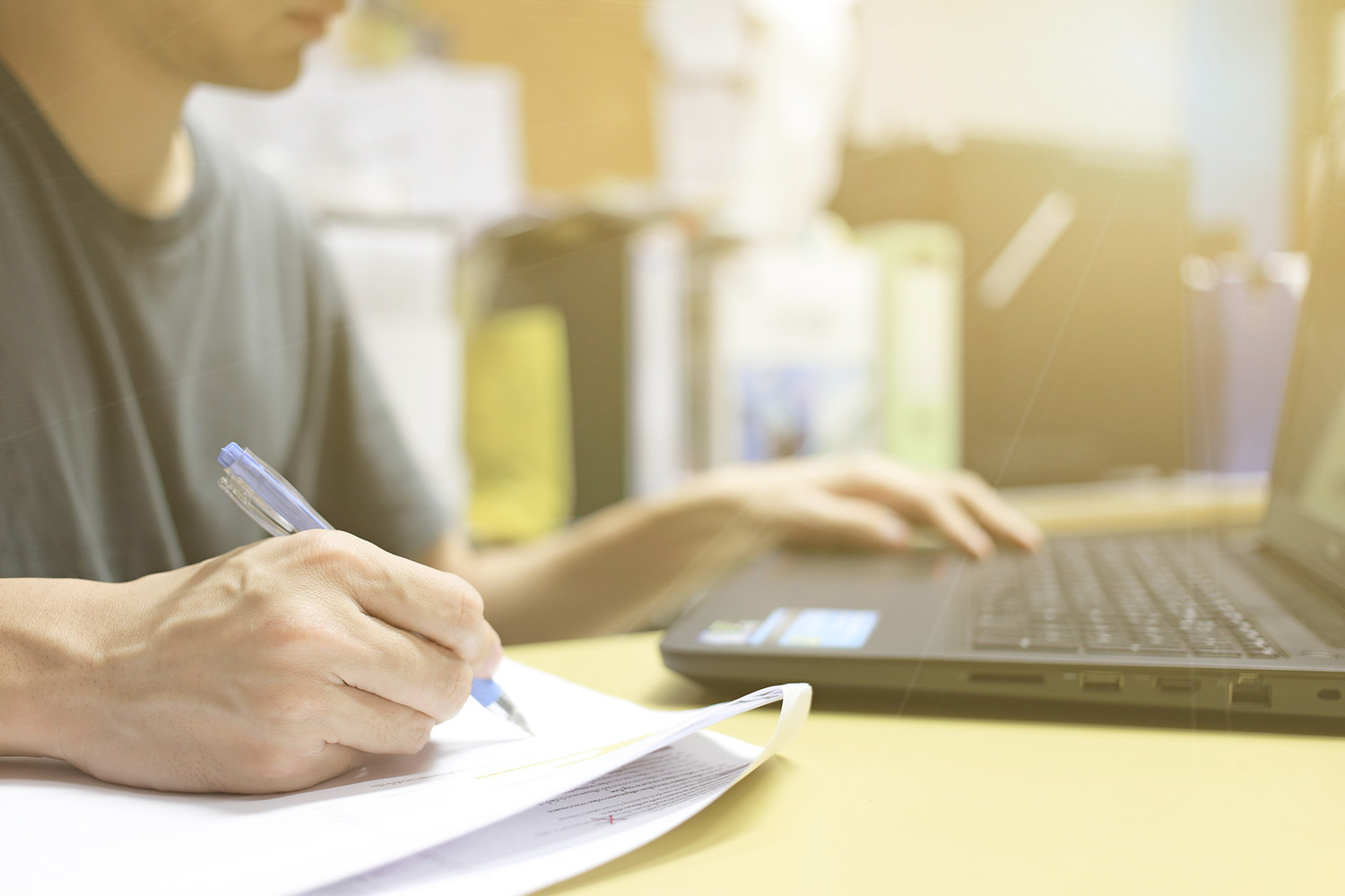 person typing and writing with a blue pen