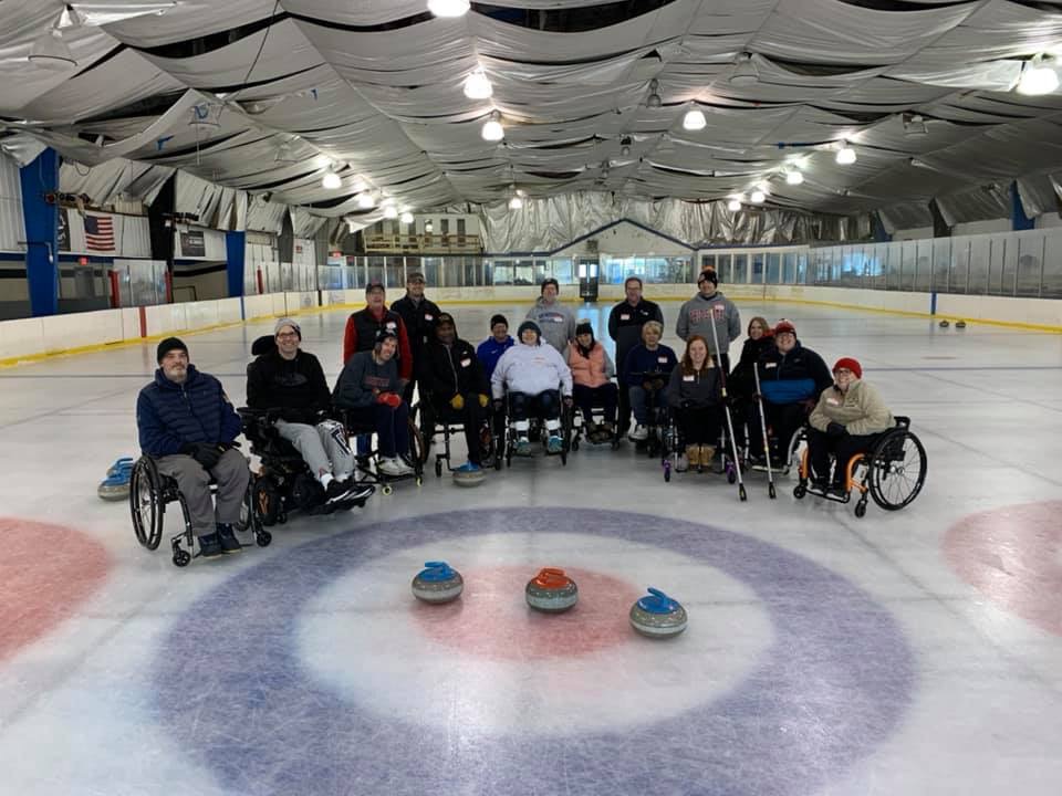 Group of happy people in wheelchairs sitting on curling ice rink