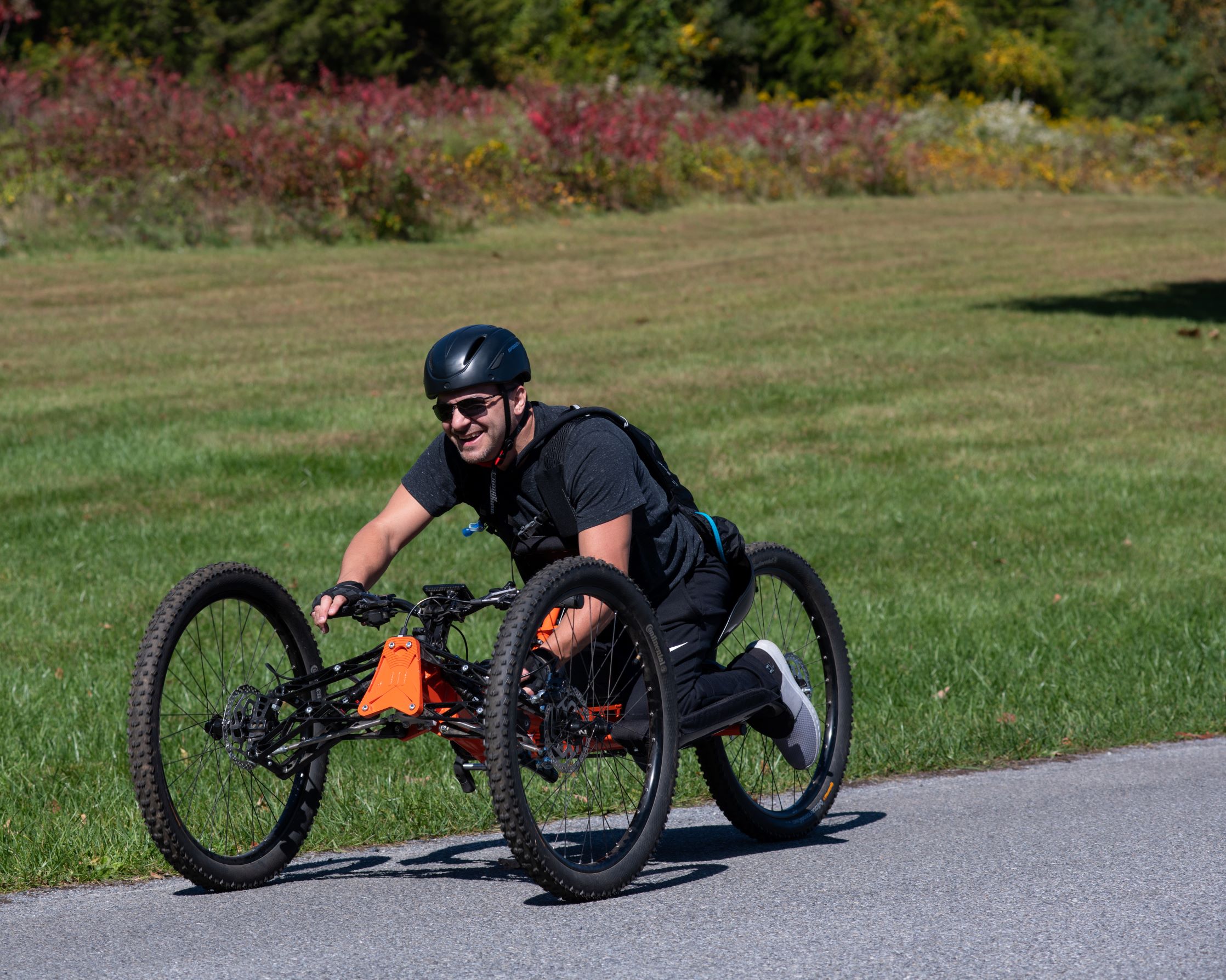 A man pedals down a road using an adaptive bicycle against a background of a green field