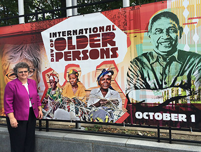 Photo of Kathy Greenlee at a mural near the UN showing 'International Day of Older Persons, October 1'